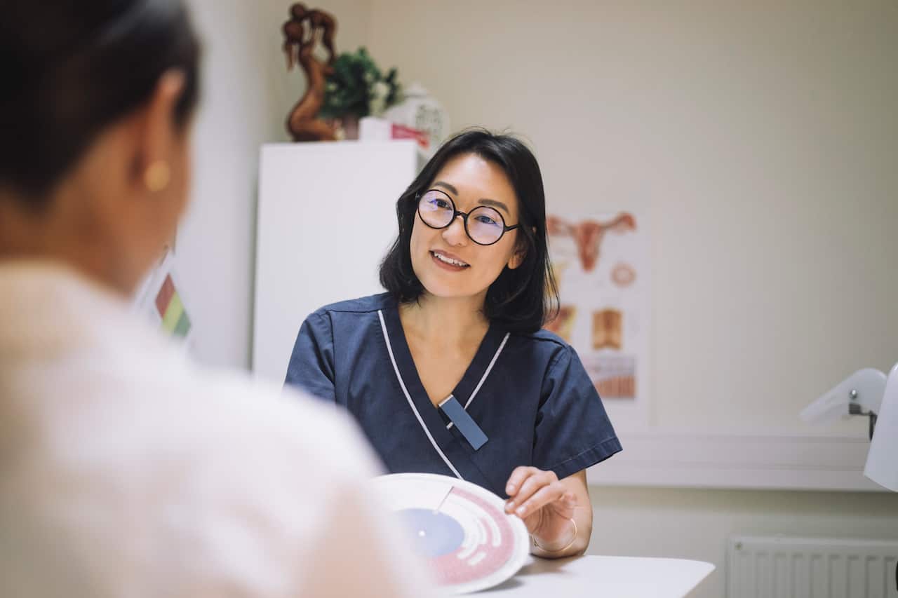 Smiling female healthcare worker showing in vitro fertilization chart while discussing with patient in clinic