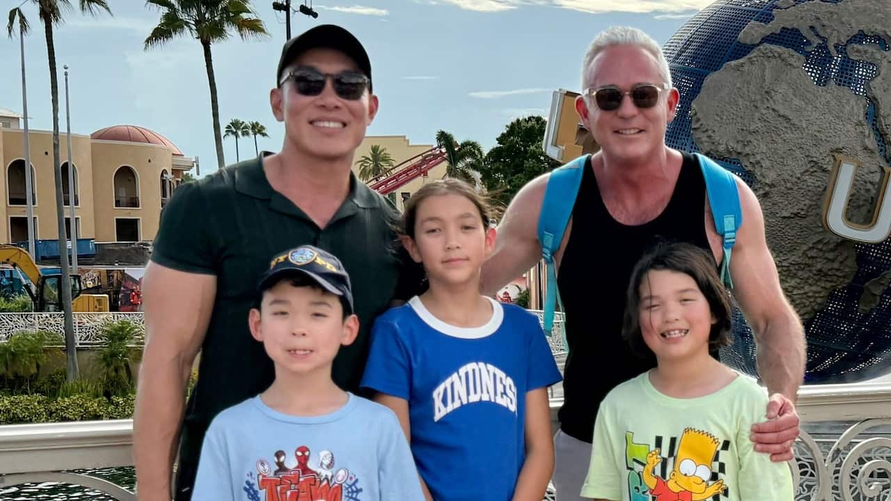 two dads with their three young kids smile for a photo in a theme park