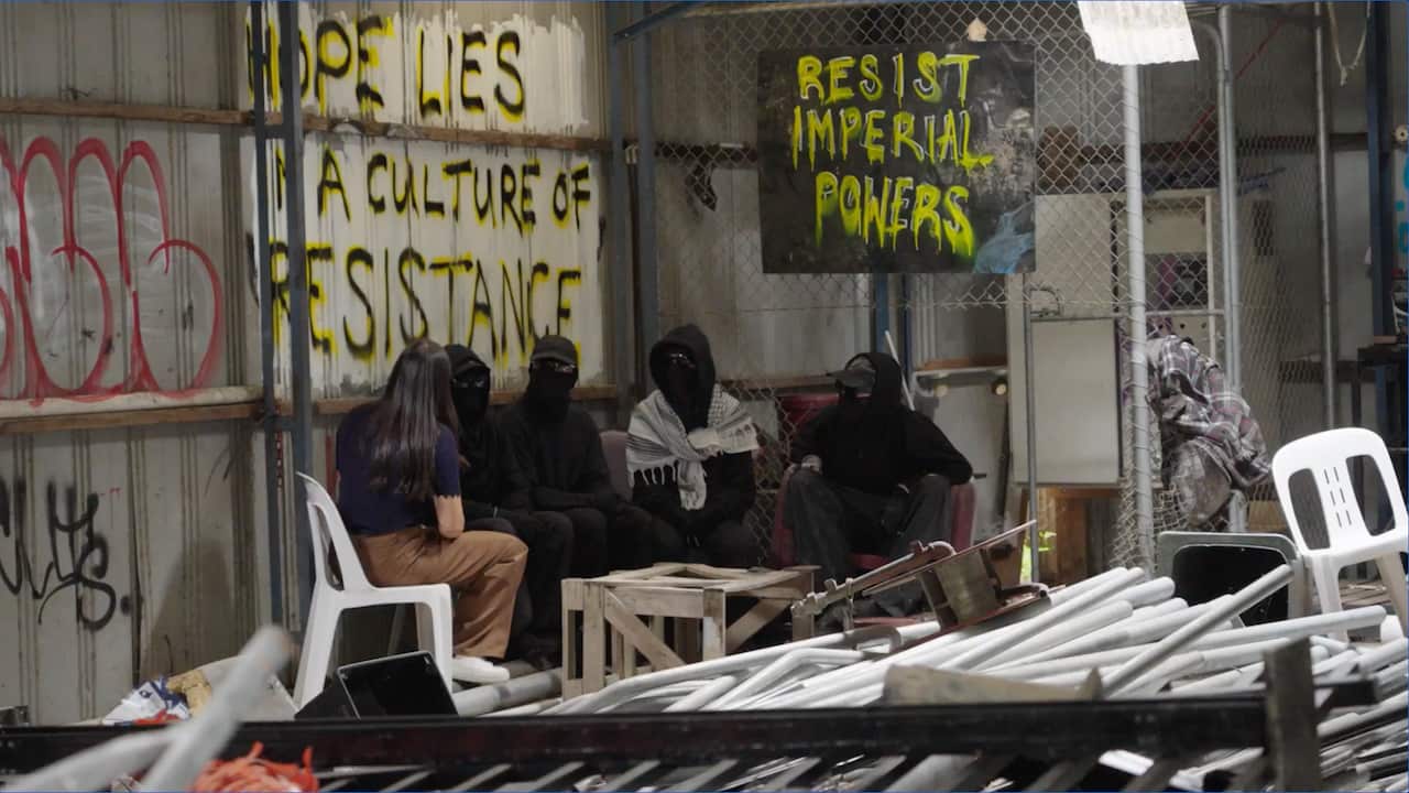 People with face coverings and glasses and one without sit in front of a mural.