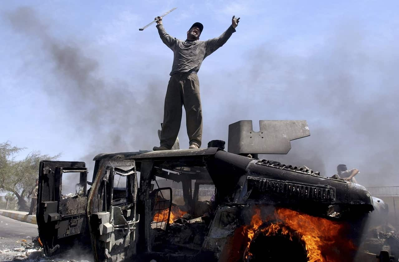 An Iraqi man on top of a burning army vehicle in 2004 