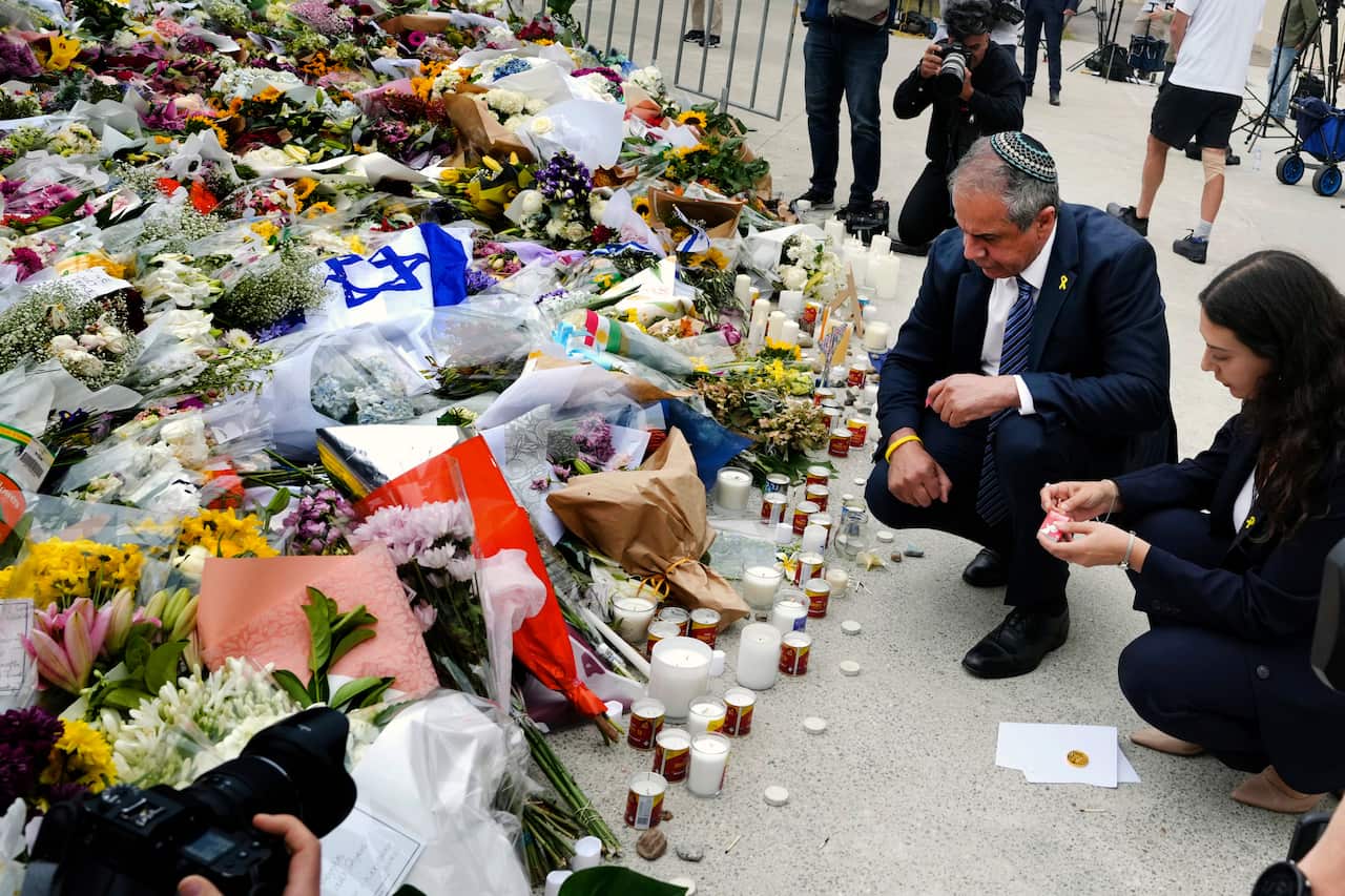 A man and woman kneeling beside floral tributes.