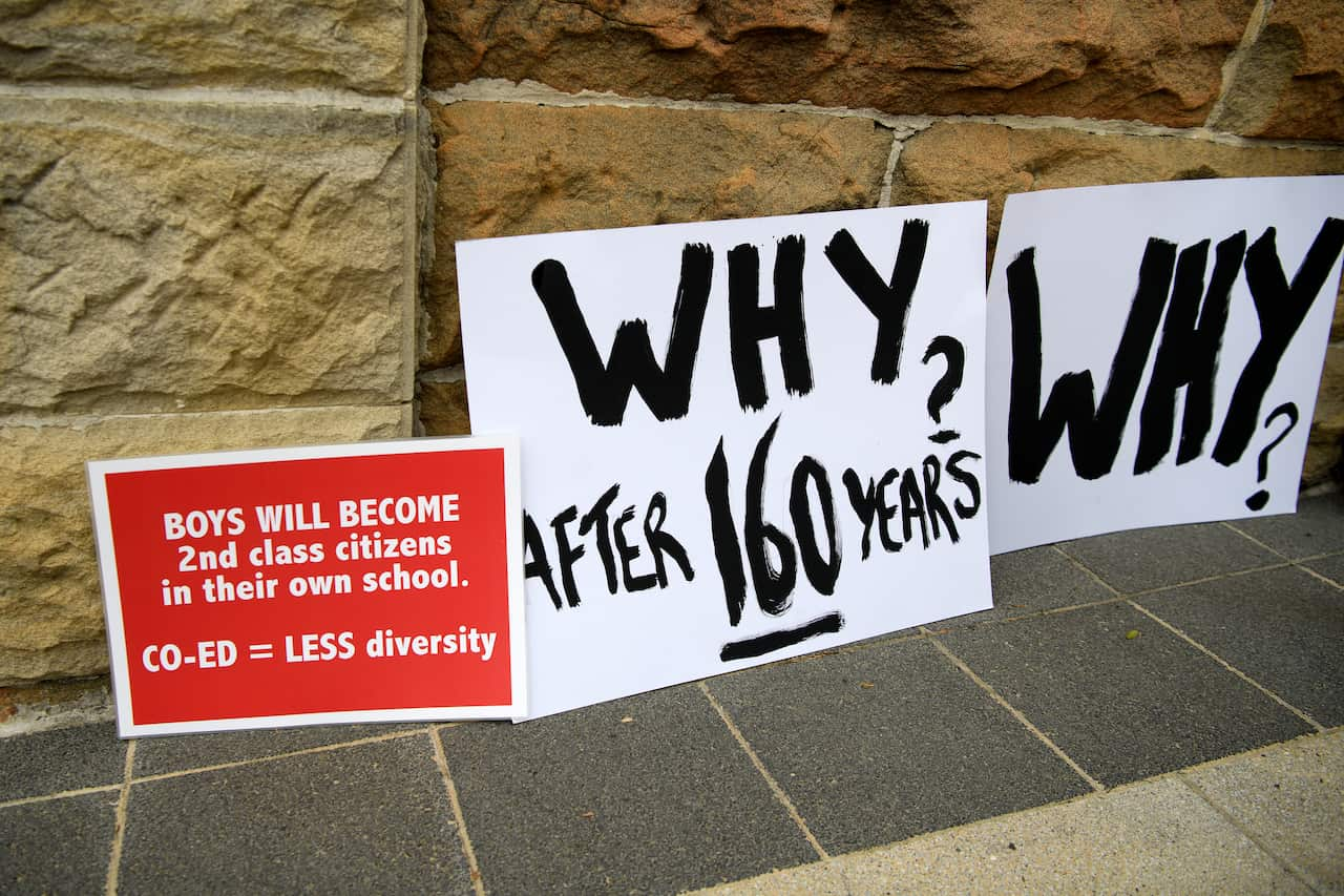 Three placards against a wall. One reads: 'Boys will become 2nd class citizens in their own school. CO-ED=LESS diversity. The others read: Why after 160 years? and Why?