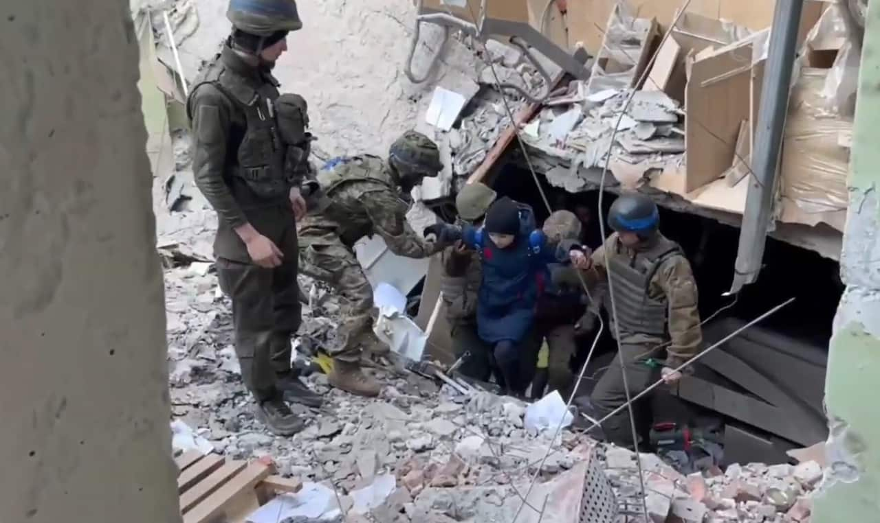 Person being escorted from rubble by soldiers. 