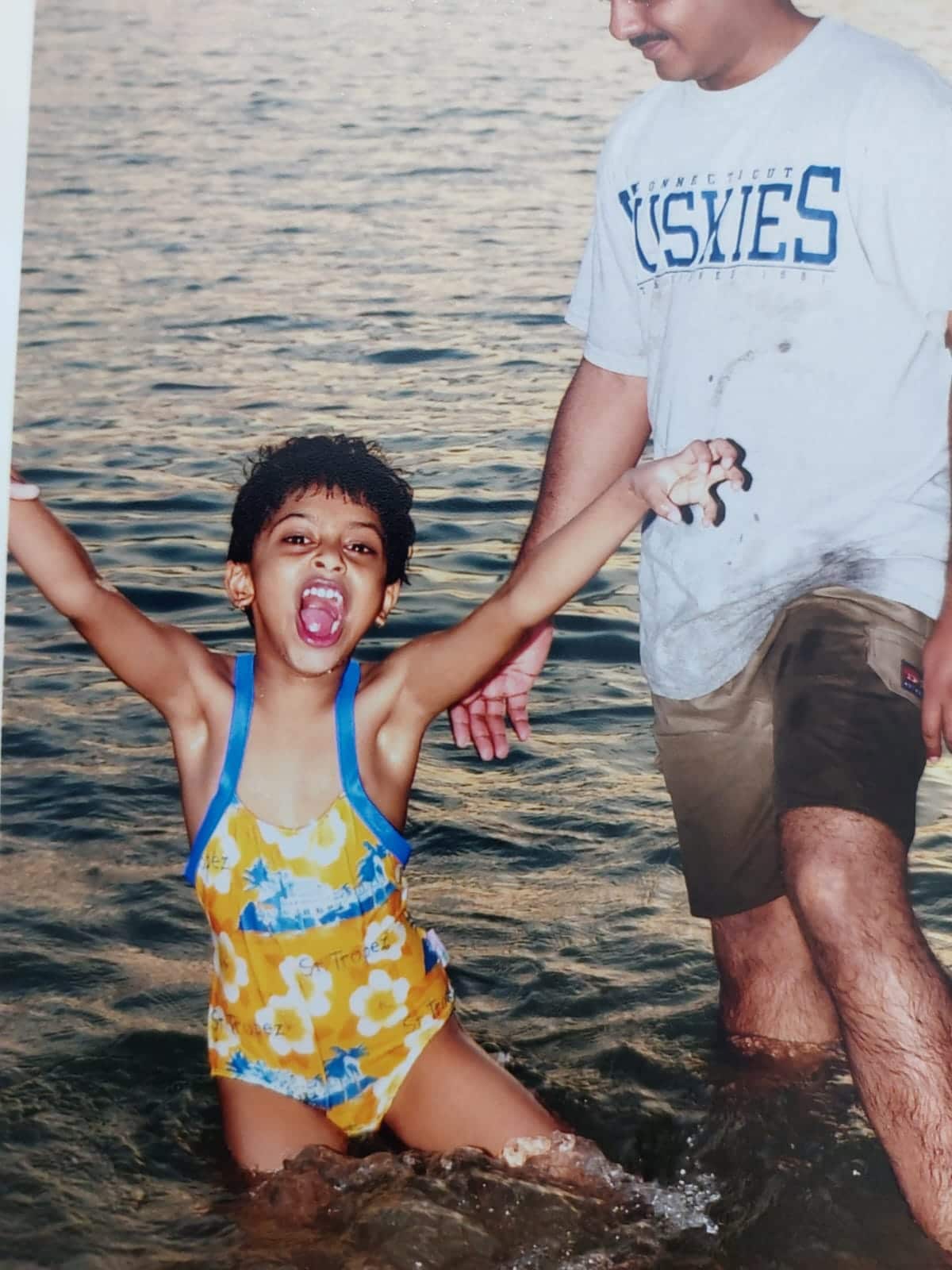 A girl stands in the water in her swimsuit and smiles.