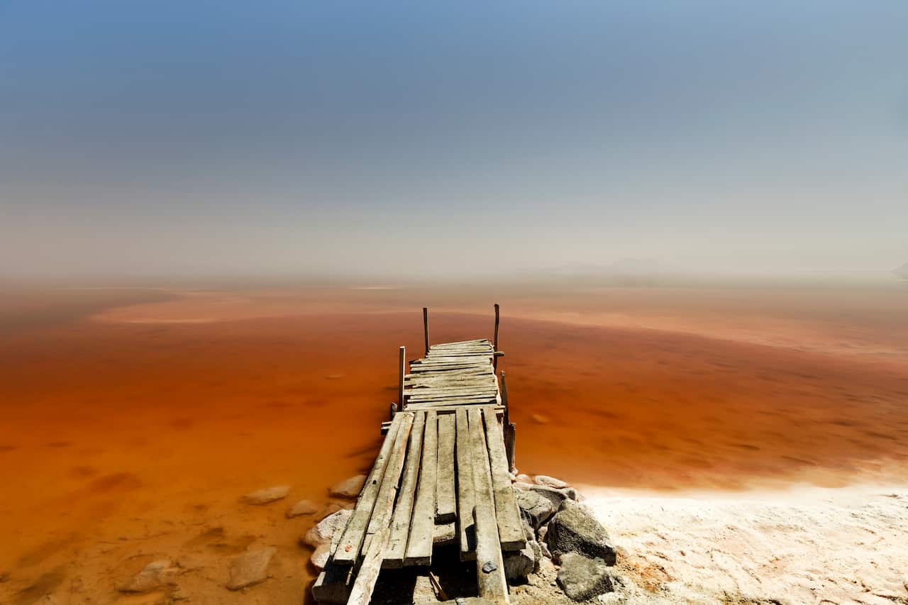 A wooden pier in a largely dried-up lake.