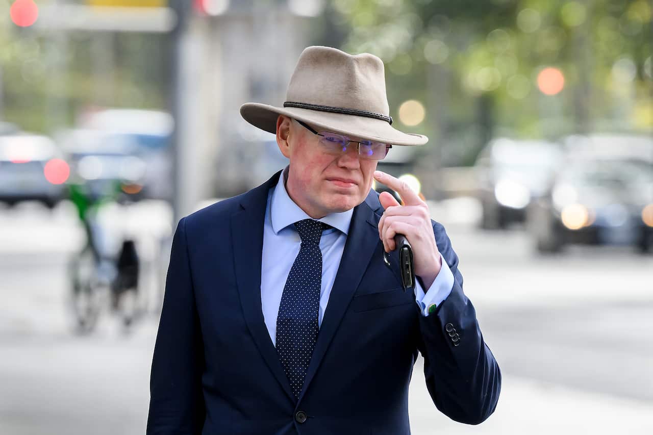 A man wearing a suit and a hat waits outside a court.