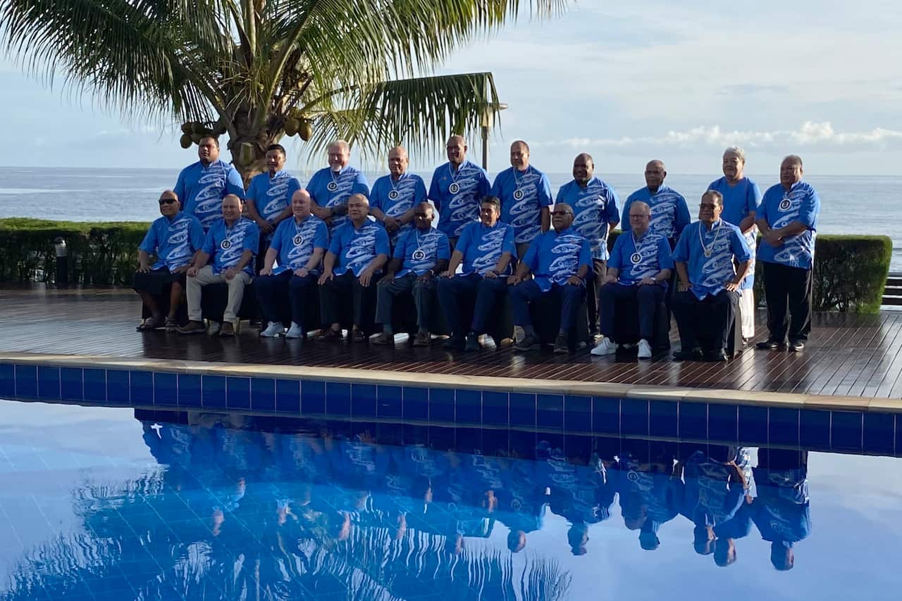 Men wearing blue t-shirts pose for a photo in front of a pool.