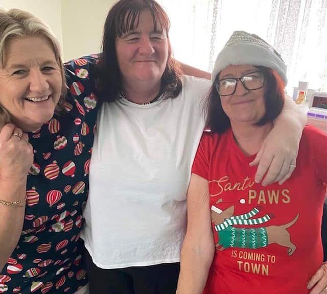 Three women pictured smiling for a photo with their arms around one another.