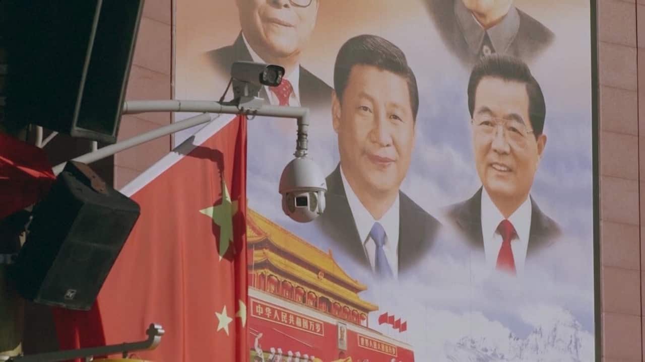 A surveillance camera is in front of a Chinese Communist Party poster that features painted images of Chinese President Xi Jinping and three other men