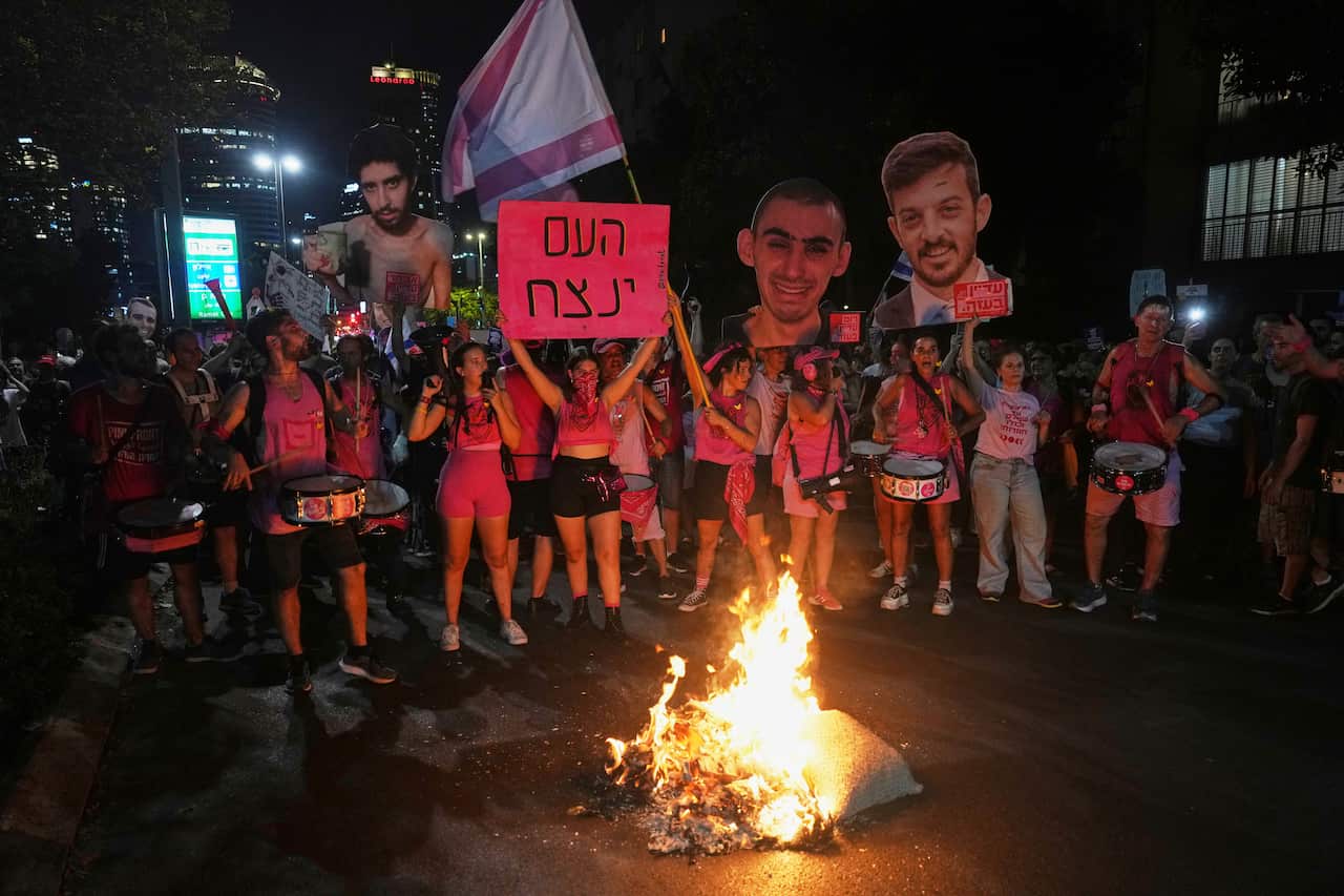 A group of protesters, some holding up signs, standing around a small fire.