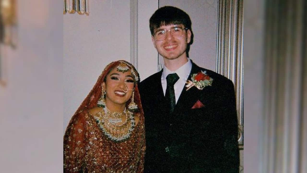 a young woman in a red and gold traditional Pakistani wedding outfit with lots of jewellery and a young man in a black suit with flowers in his pocket