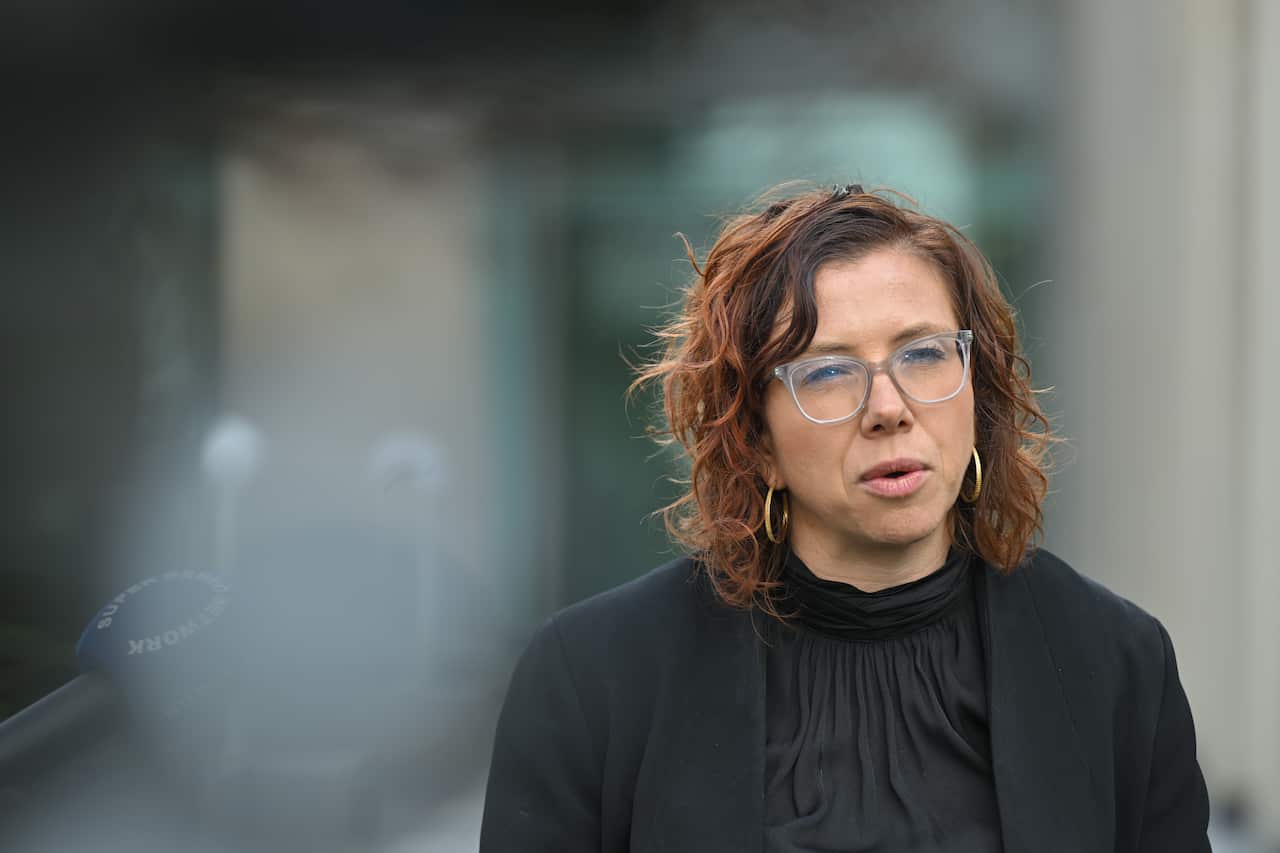 A woman in a black suit and glasses.