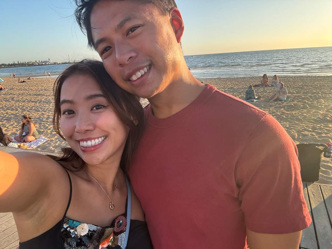 A man and a woman pose for a selfie photo by the beach.