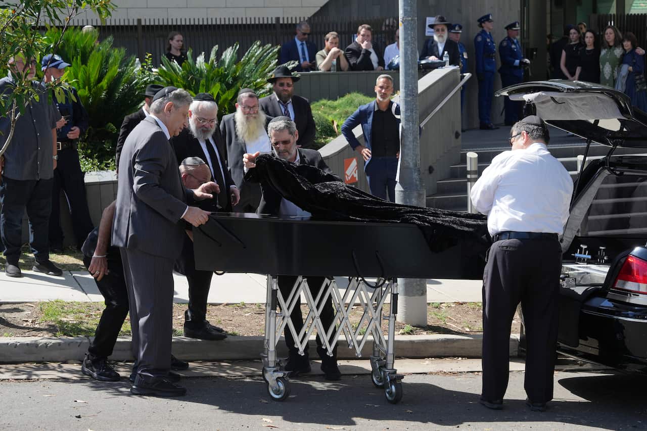 A coffin is unloaded from a hearse outside a synagogue.