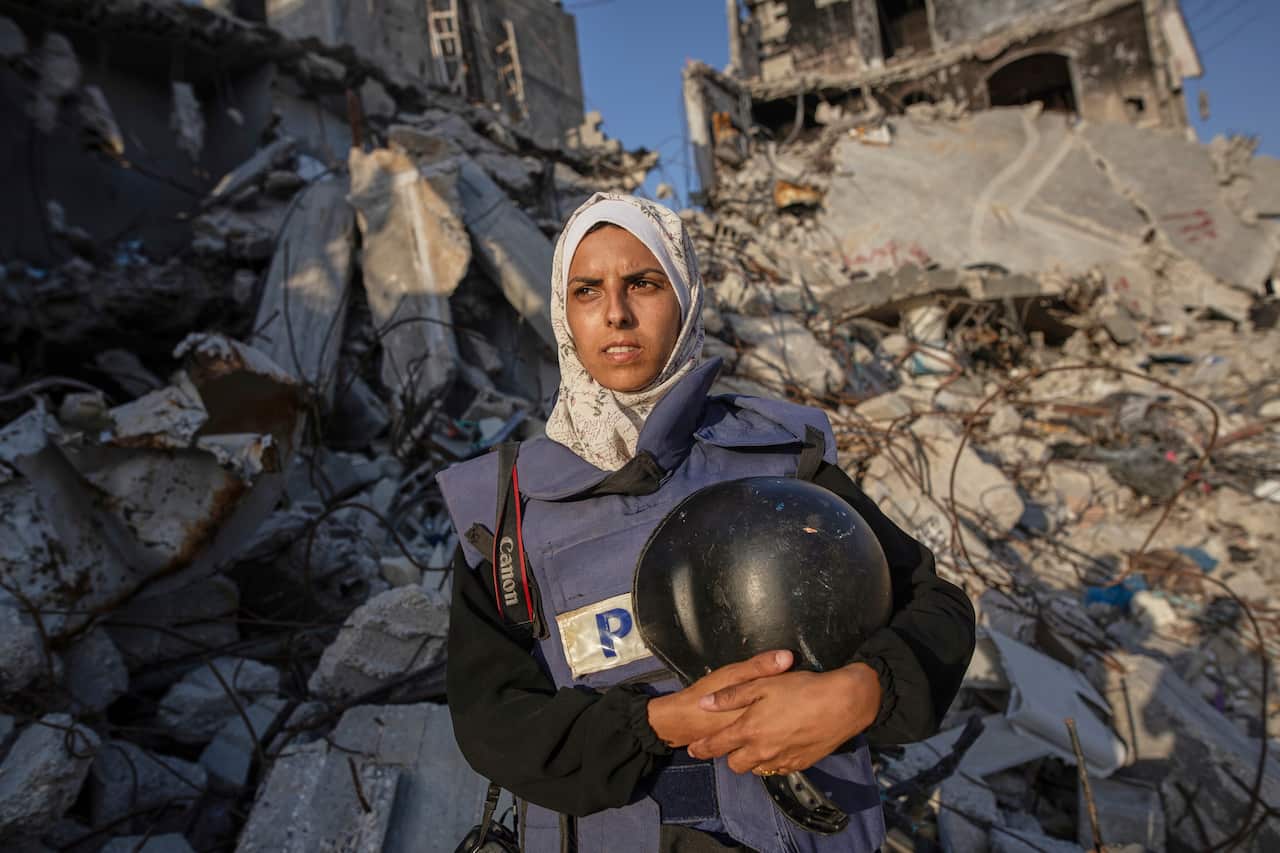 A journalist wearing a press vest poses for a photo holding a helmet.
