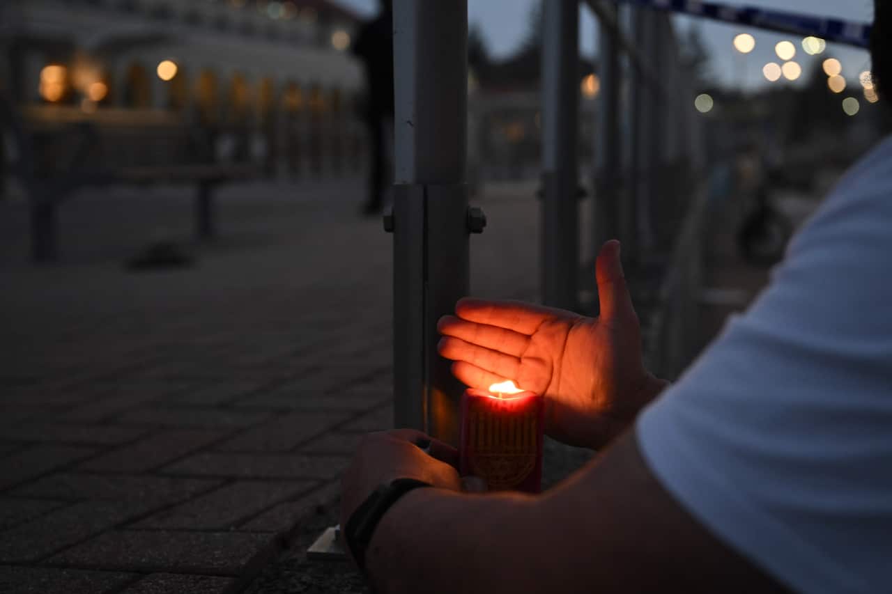 A man lays down a lit candle on a footpath.