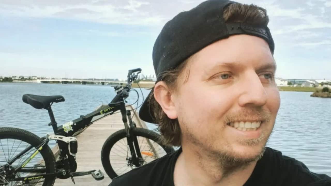 A man sitting on a jetty with his bicycle in the background smiles at the camera