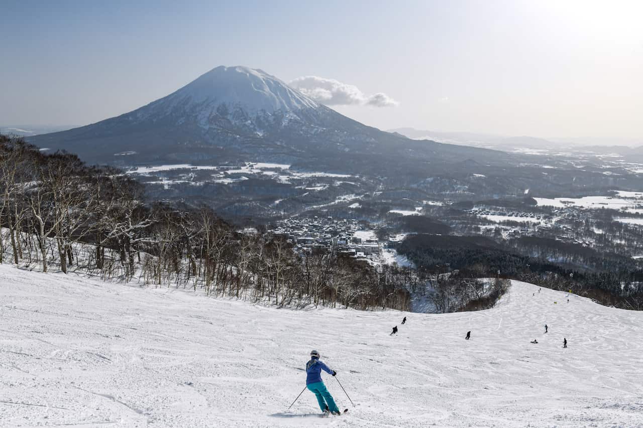 La gente conduce por una montaña cubierta de nieve; al fondo se puede ver una gran montaña con forma de volcán 