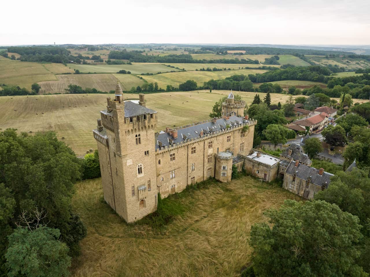 An aerial shot of a large manor house, surrounded by countryside and a small town. 