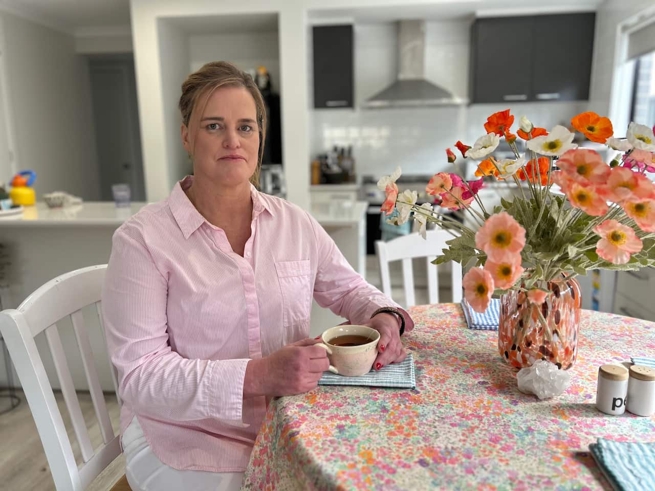 Diana sits at a table in her kitchen.