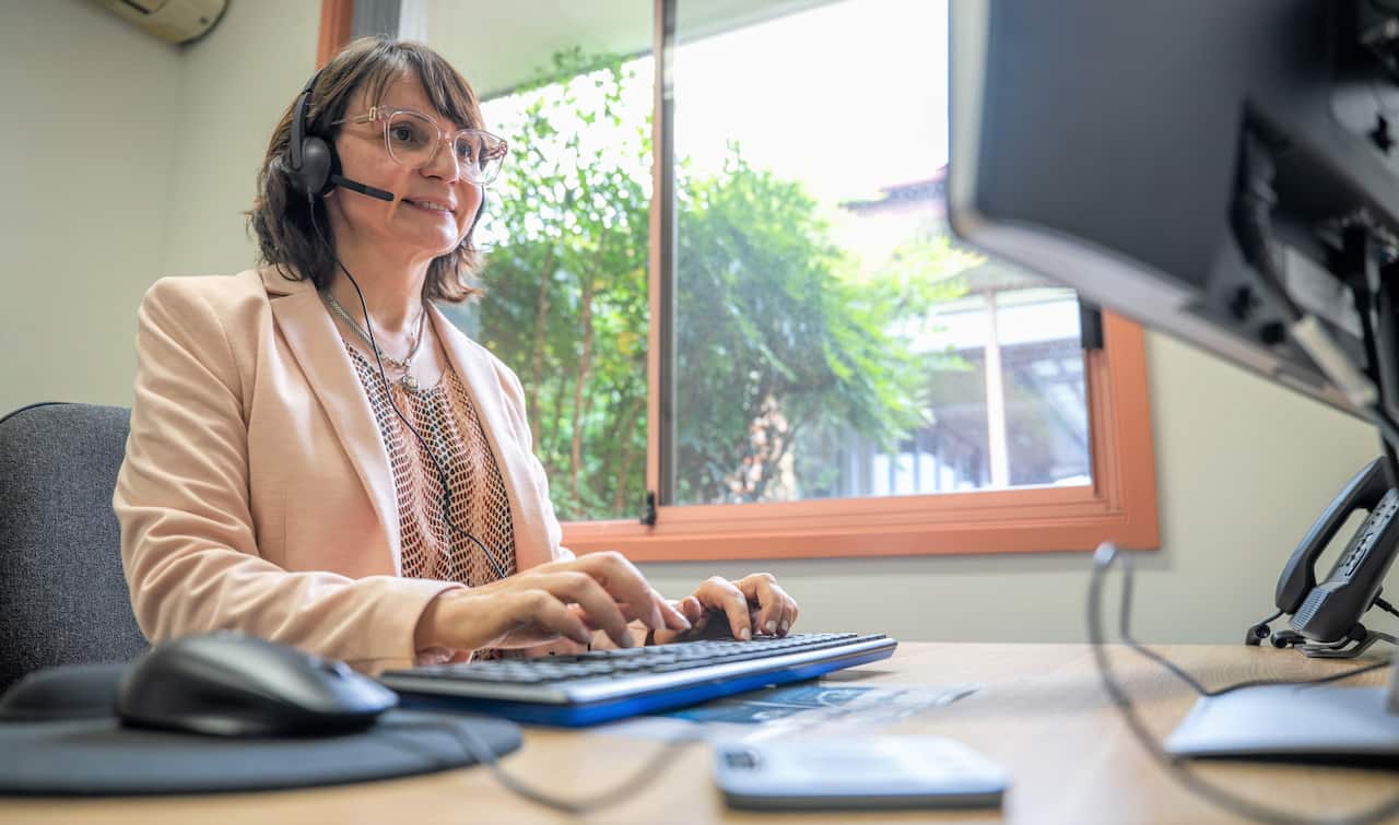 A woman wearing a headset sits at a computer with her hands on a keyboard.