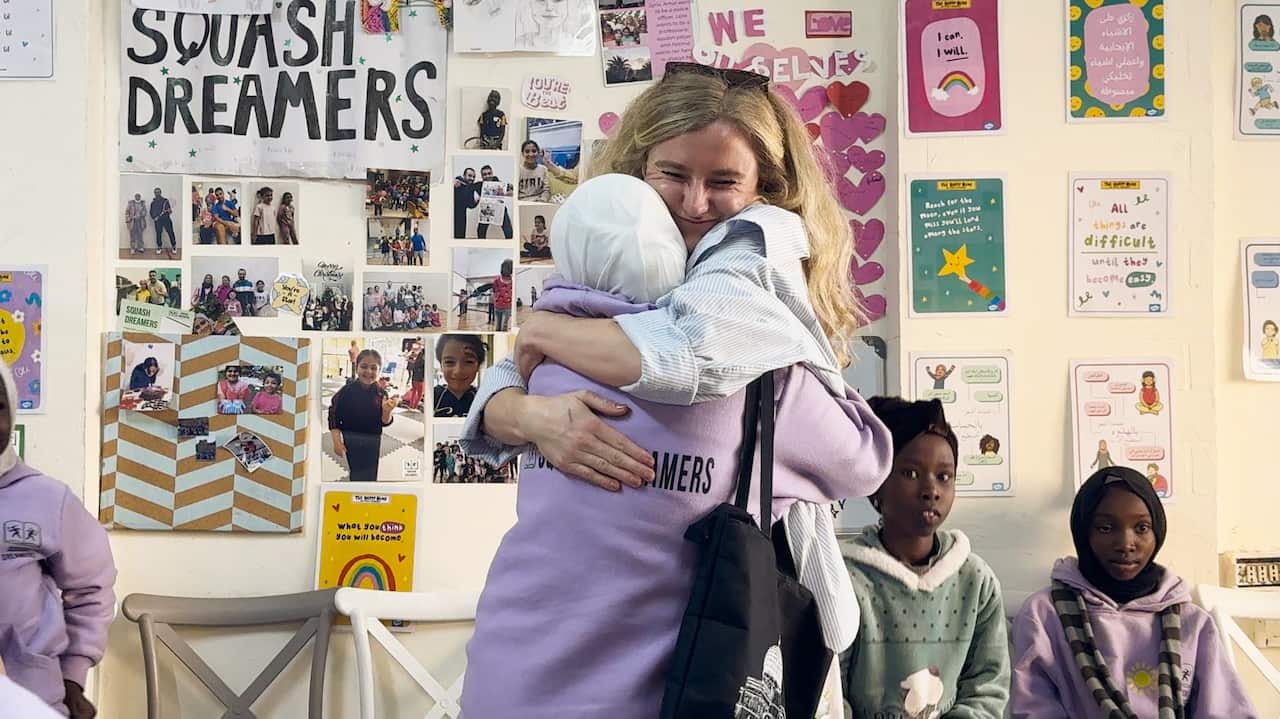 A blonde woman embraces a young girl as other girls watch on