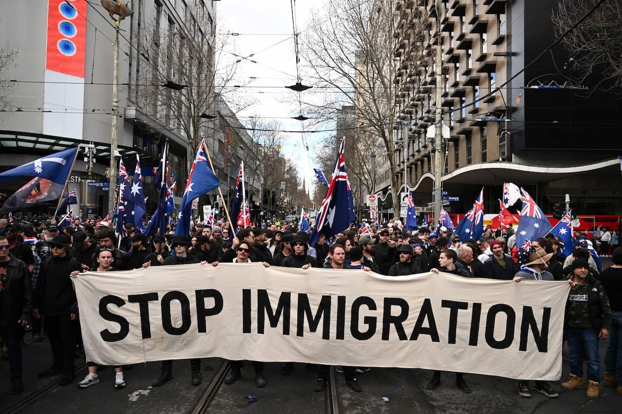 A group of protesters walking down a street carrying a sign that reads "Stop Immigration".