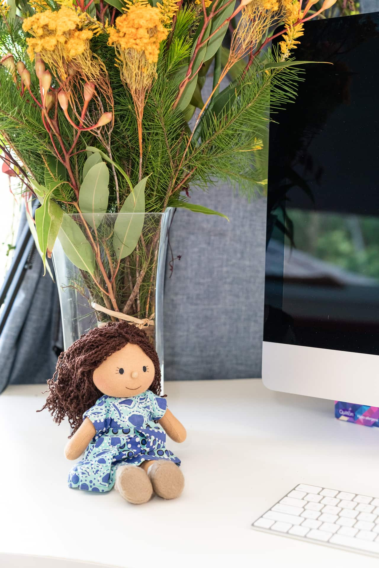 A doll sits on a desk next to a vase