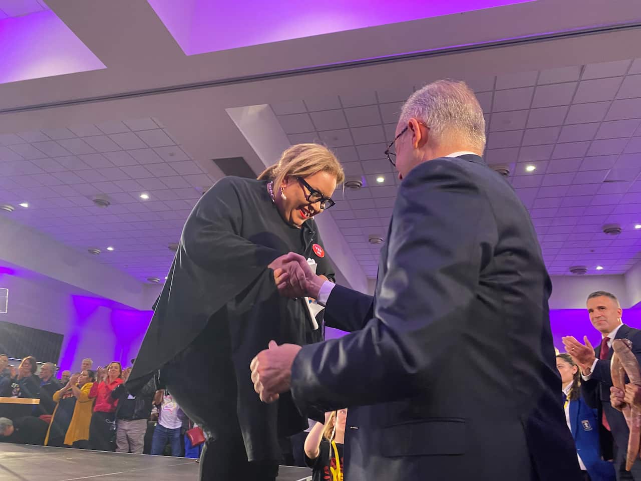 Woman smiles as the is helped off stage by a man.