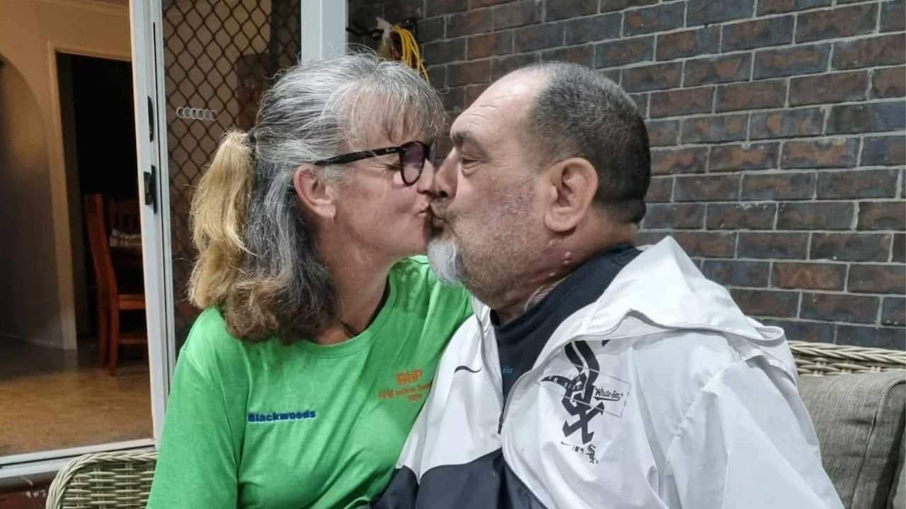 a middled aged woman in a green tshirt and middle aged man in white sox jacket kiss on an outdoor lounge on a patio