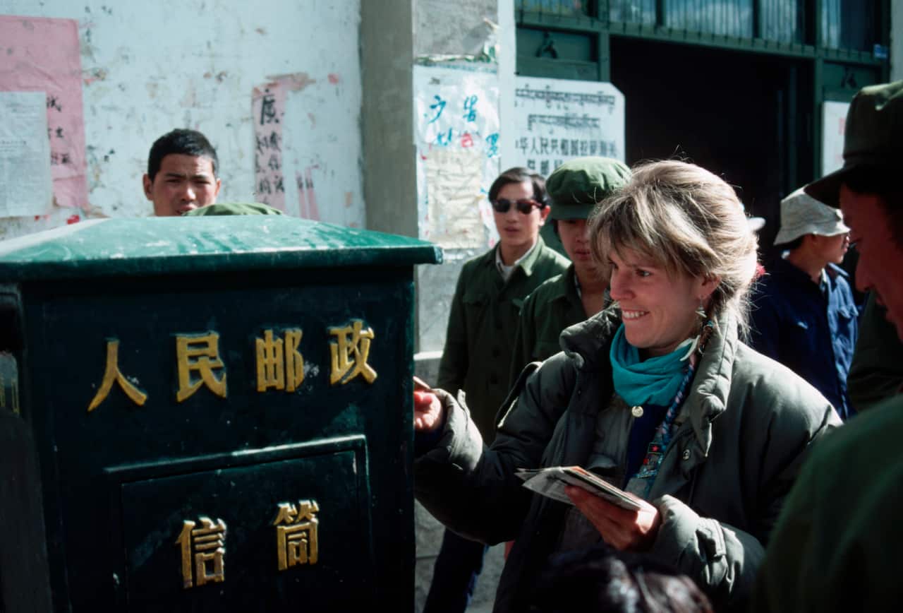 Curious Bystanders Watch Tourist Mail Postcards in Tibet
