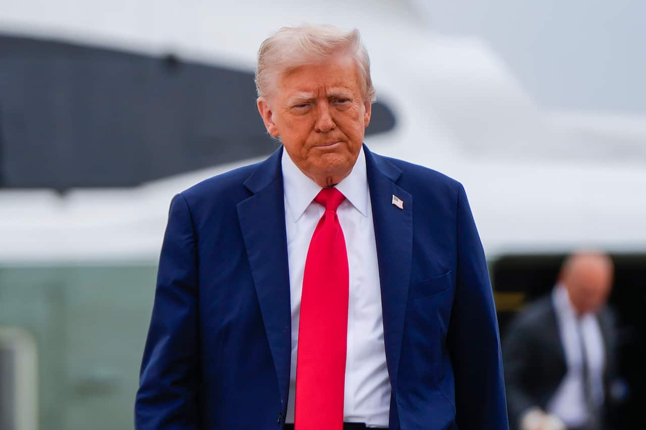 Donald Trump, wearing a blue suit with an American flag pin on it, white shirt and red tie.