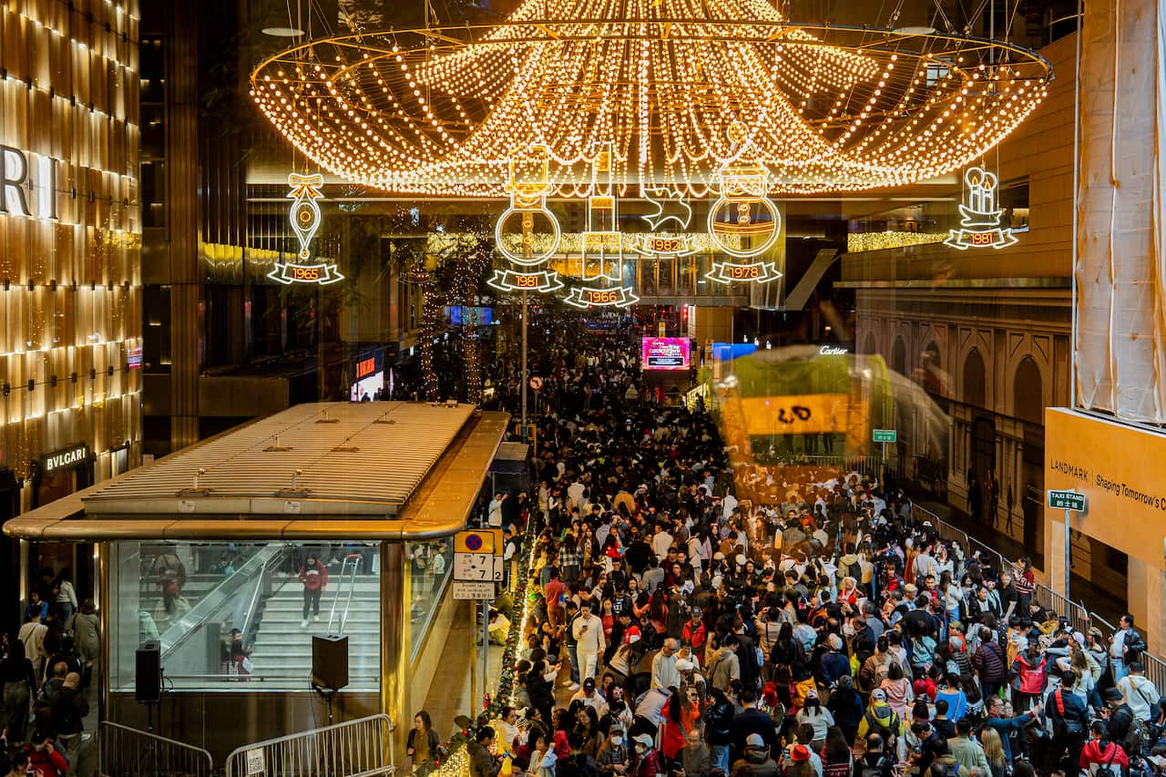 Packed crowds in a festively-lit city street near a subway entrance.