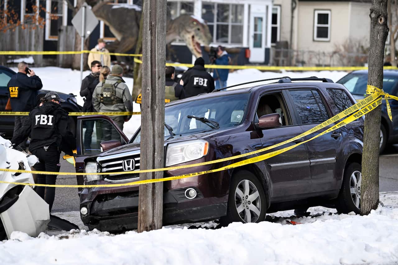 Agents with FBI uniforms and other law enforcement gather near a crashed vehicle in a snowy area surrounded by police tape.