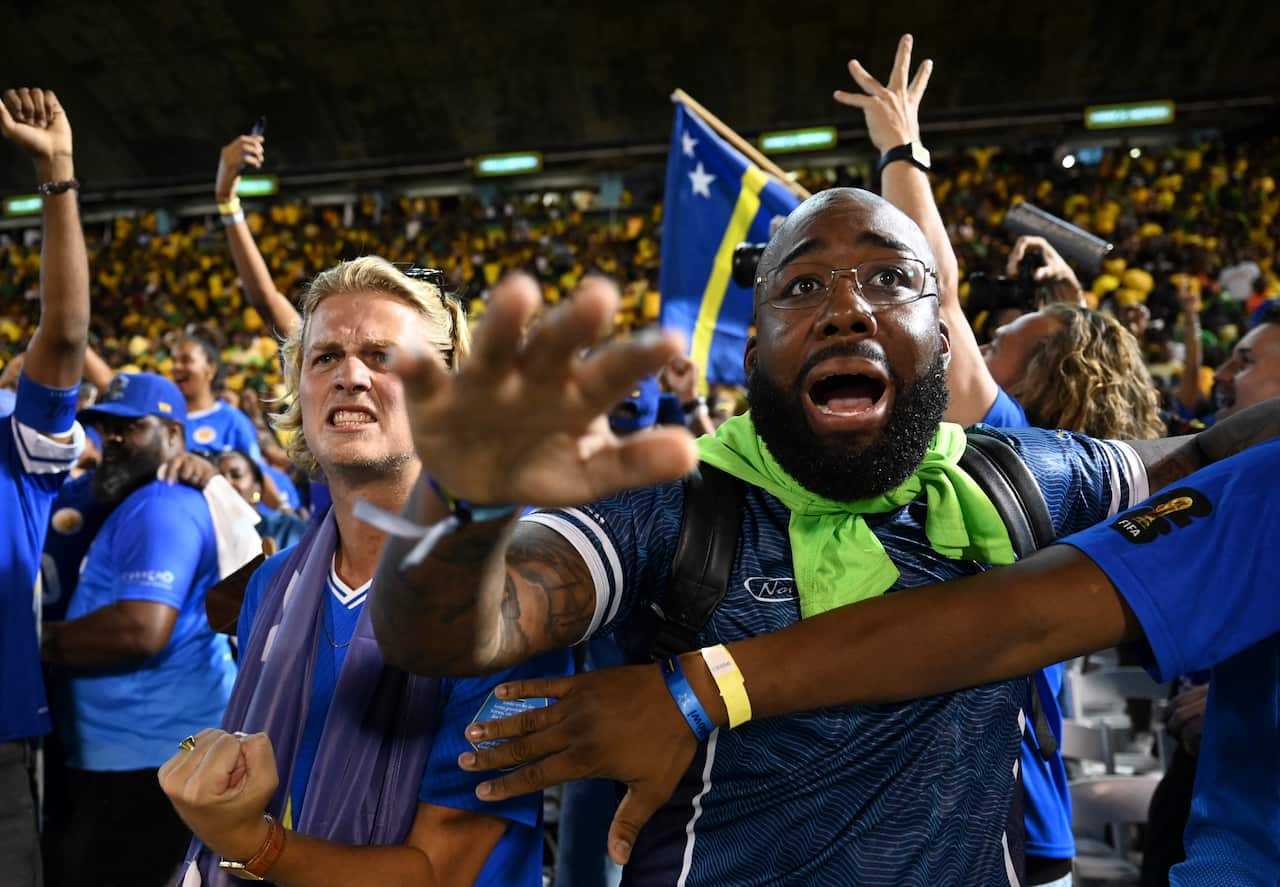 Football fans wearing blue shirts celebrate in a stadium