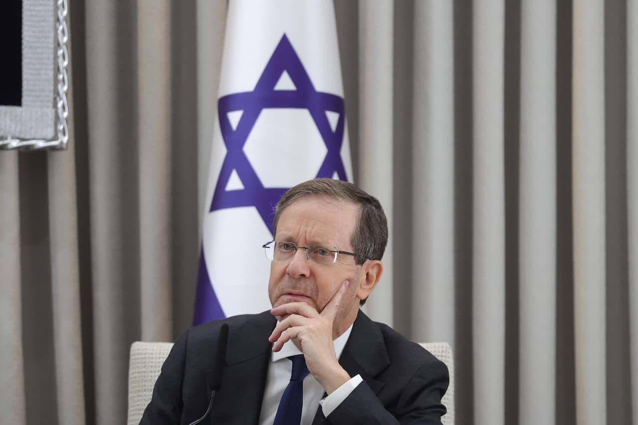 A middle-aged white man wearing glasses and a suit. An Israeli flag is behind him.