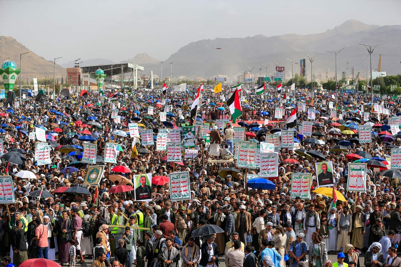 A large crowd holds up signs and umbrellas.