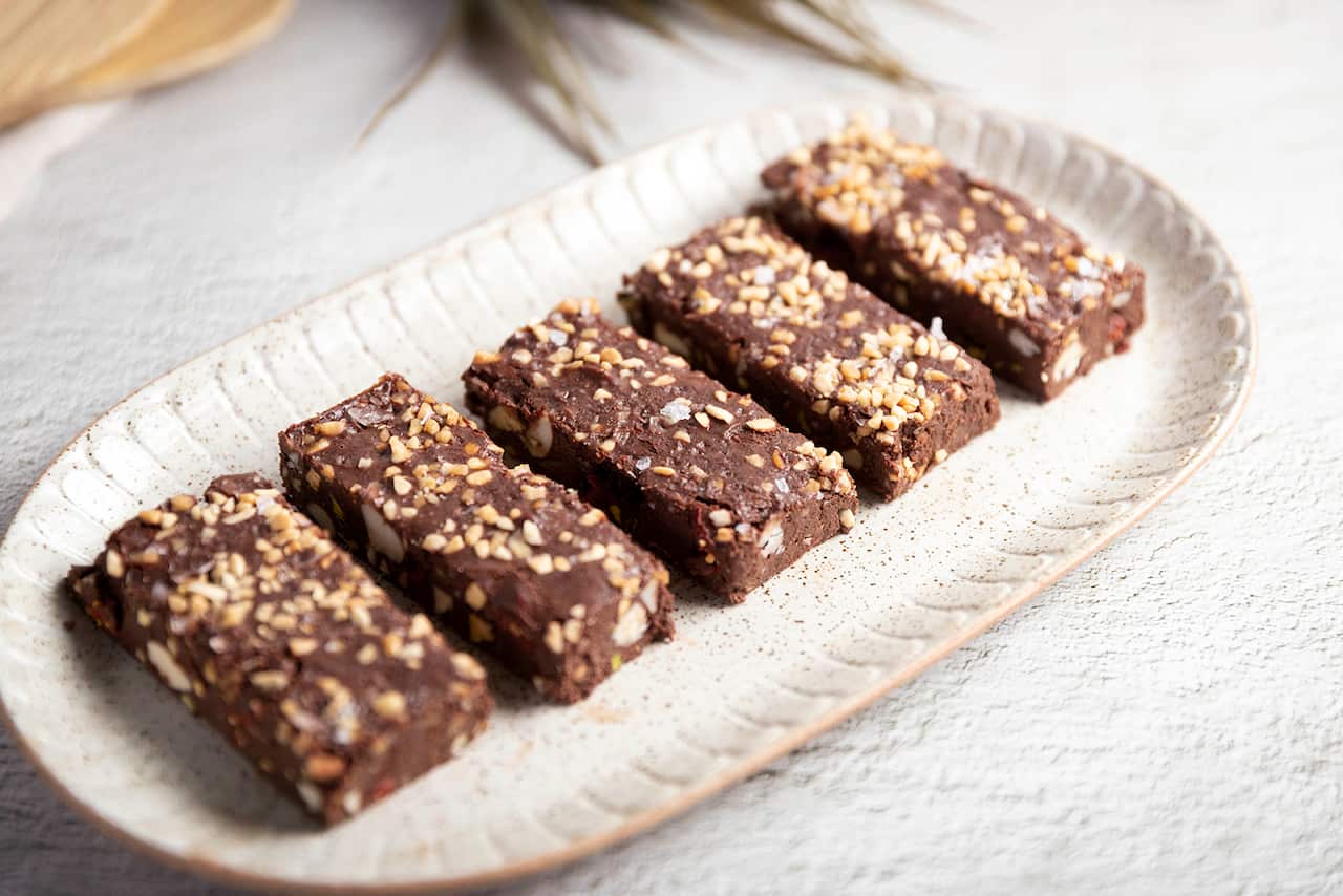 Five pices of rocky road, sprinkled with crushed peanuts, sit on a pale oval platter with decoratively marked edges. 