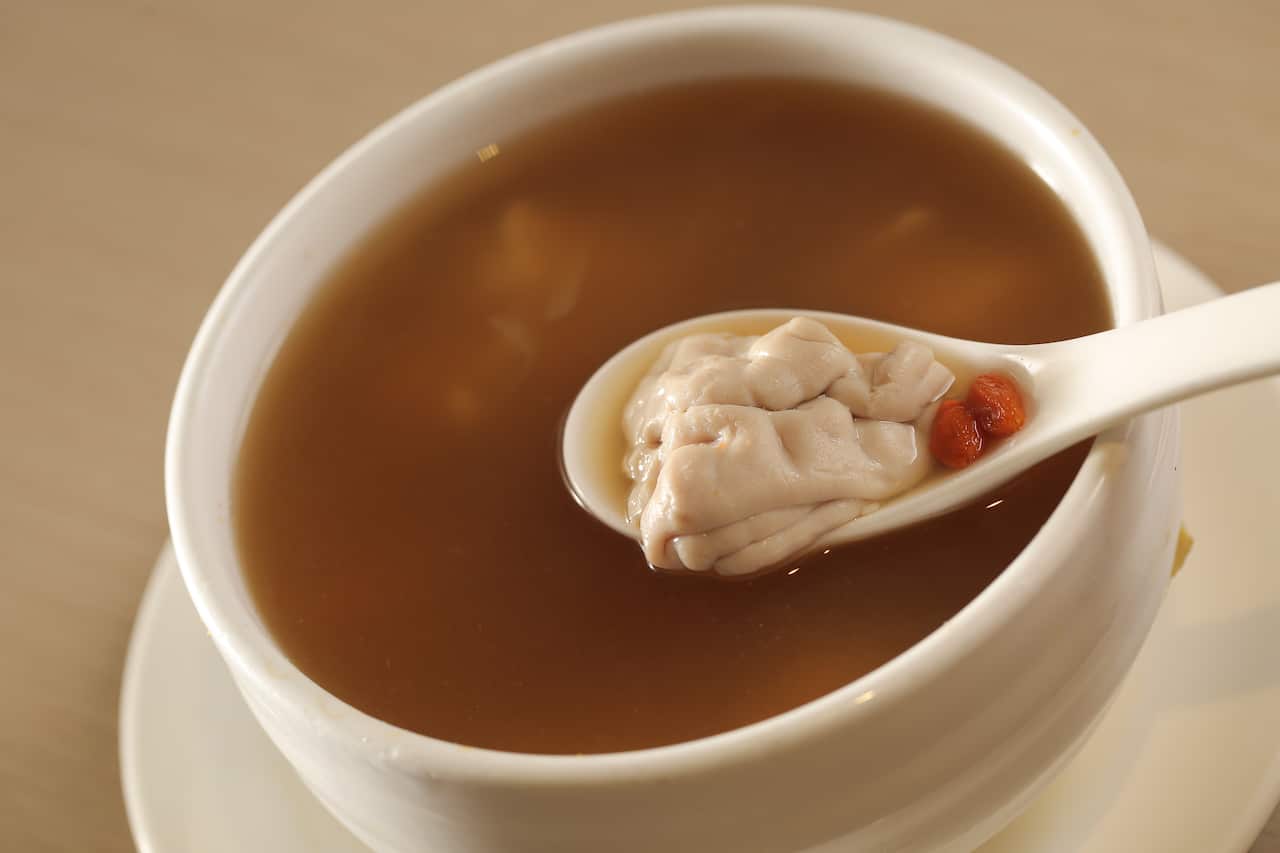 A clear broth in a white bowl with a traditional Chinese spoon with some white ingredients and small berries