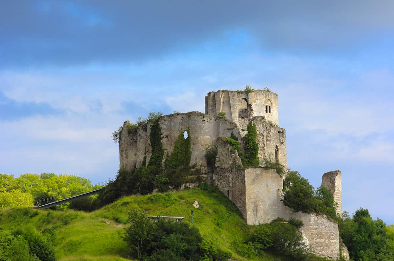 Ruins of a medieval castle sit on top of a grassy hill.