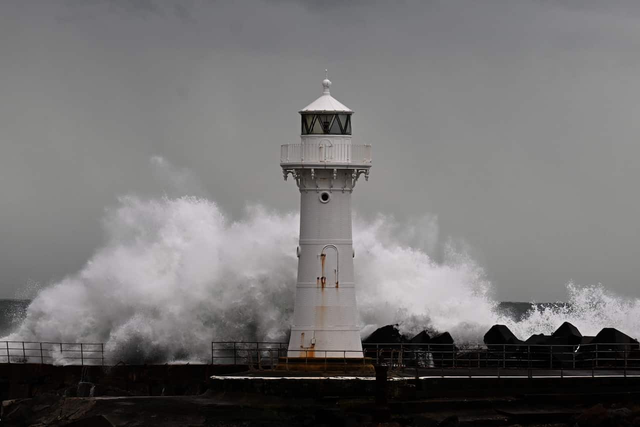White lighthouse with crashing waves in stormy weather.