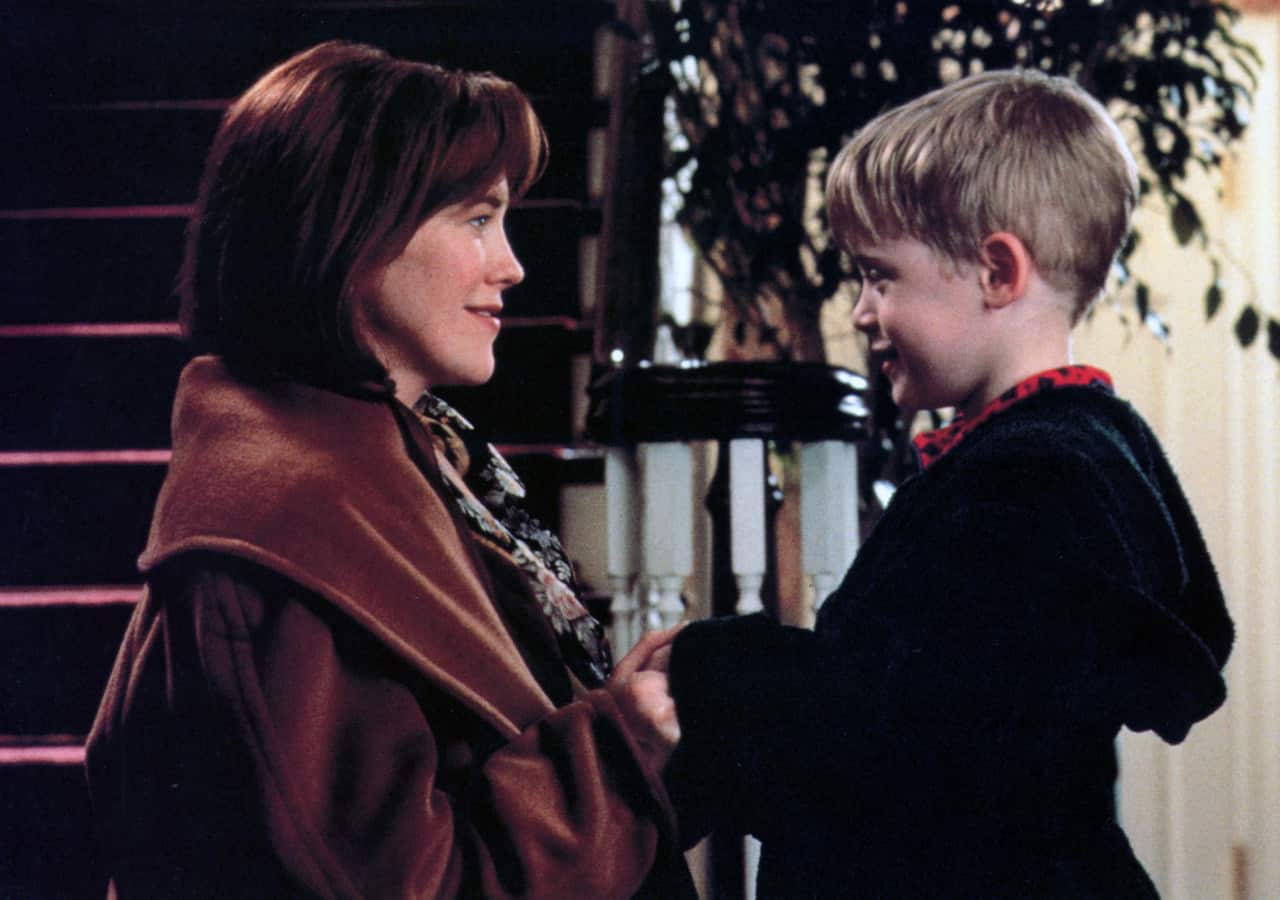 Una mujer y un niño se enfrentan cerca de una escalera en el interior, tomados de la mano y sonriendo