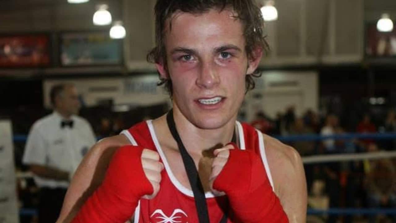 a teenage boy in red singlet and gloves poses in a sparring pose and has a medal around his neck