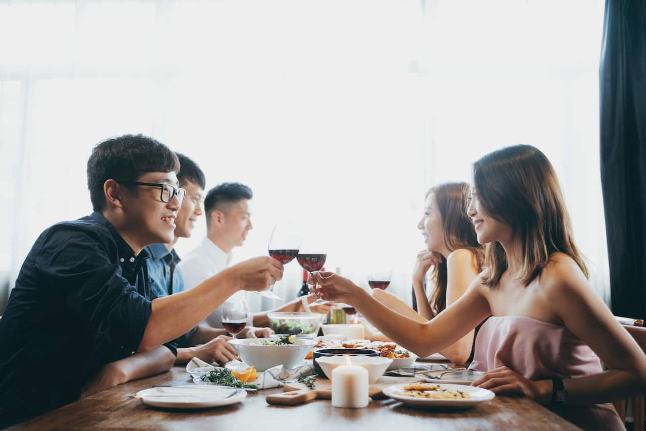 Group of joyful young Asian man and woman chatting, having fun and toasting with red wine during party