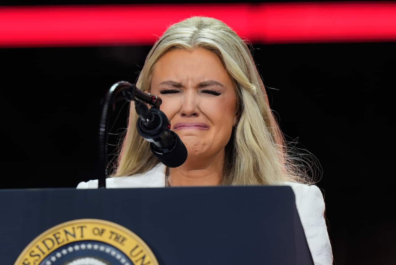 A woman with long blonde hair crying behind a podium