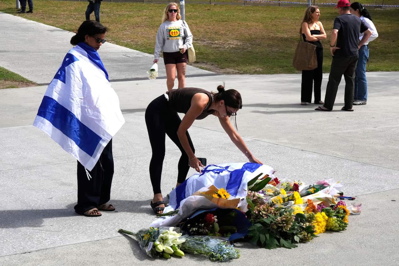 A woman places an Israeli flag over flowers outside Bondi Pavilion.