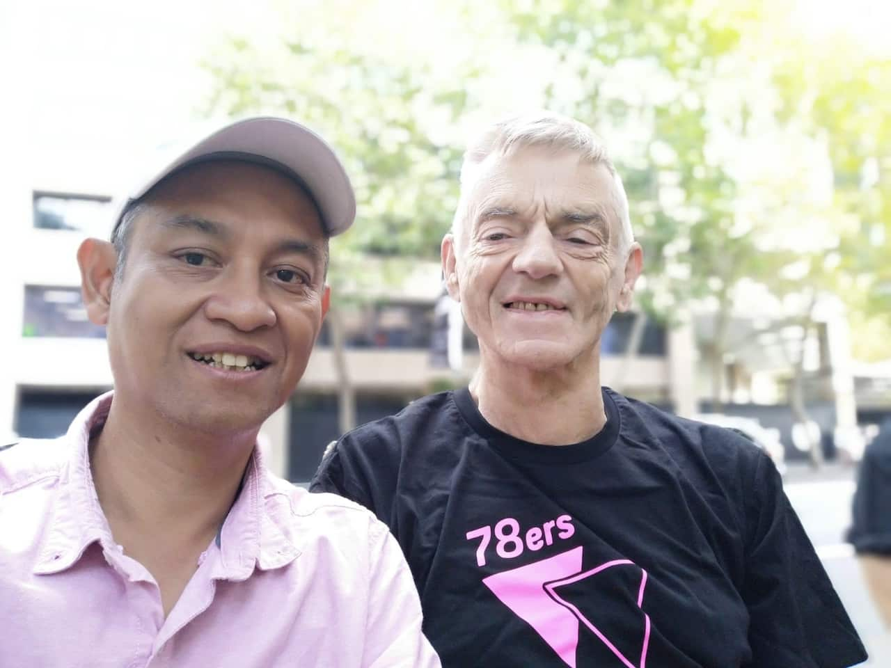 A man wearing a pink shirt next to a man wearing a black shirt. 