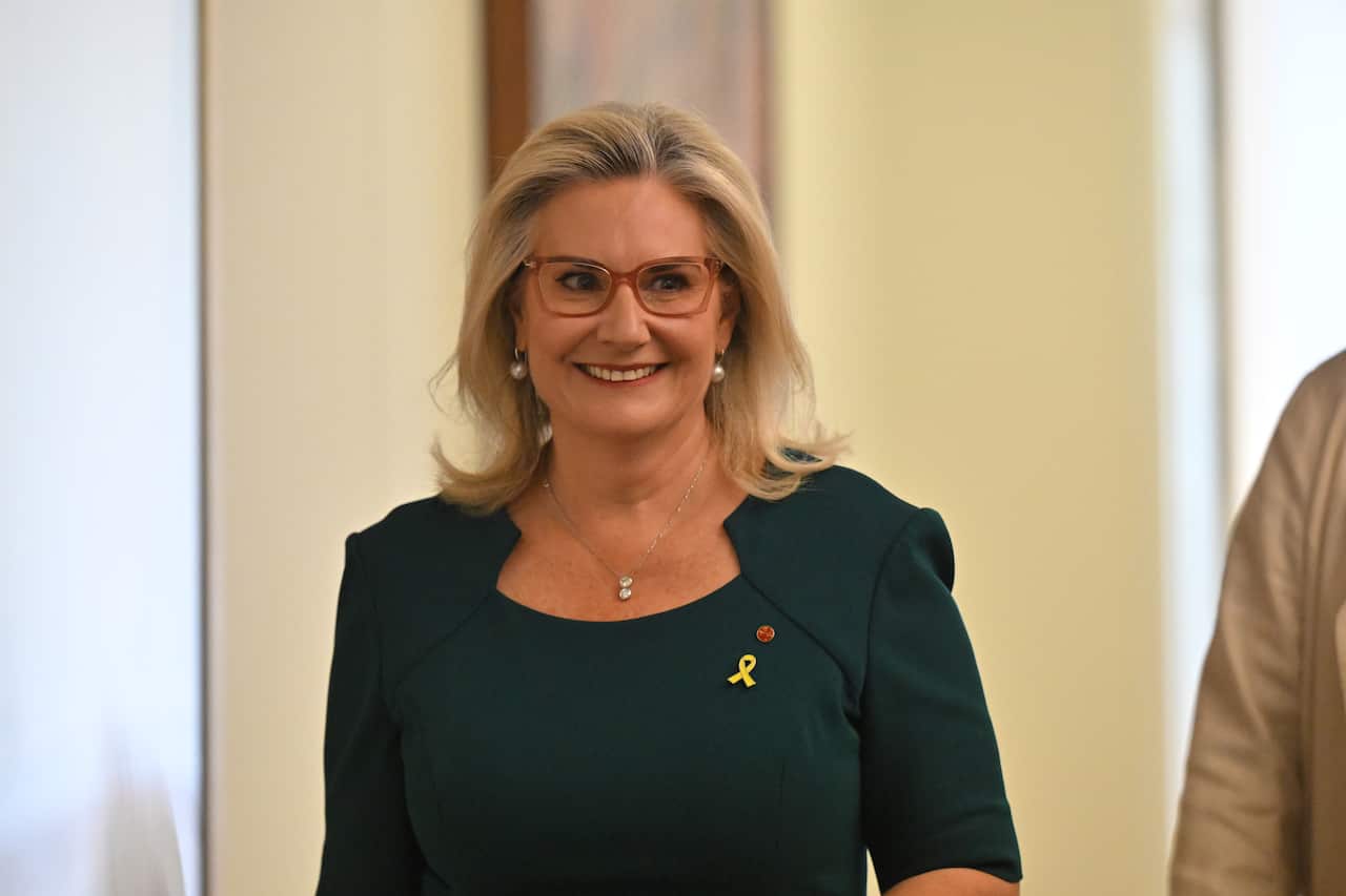 A middle-aged white woman with blonde hair and glasses is smiling.