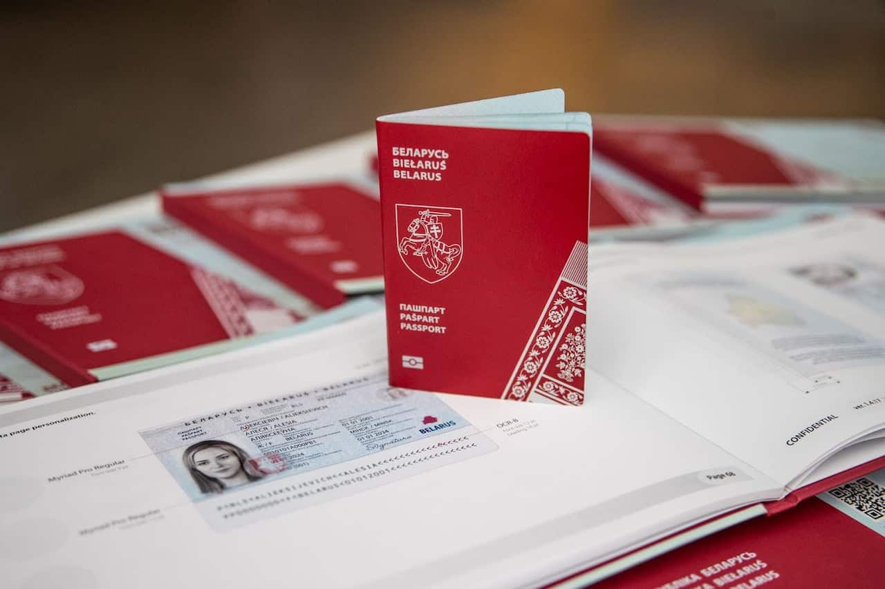 A passport with a red cover and the coat of arms is shown standing open on a white table, next to an open book displaying a sample data page with a woman's photo and text.