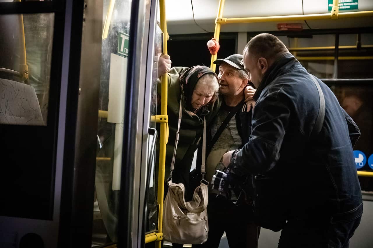 Volunteers assist an old lady to get off the bus